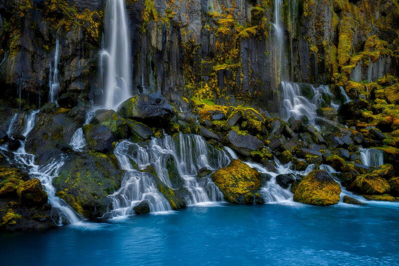 Hraunfossar's countless waterfalls emerge from ancient lava fields into brilliant blue water.