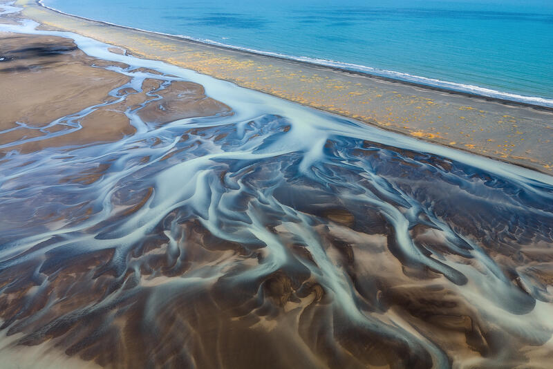 Braided glacial rivers merge toward the Atlantic along Iceland's black sand coastline.