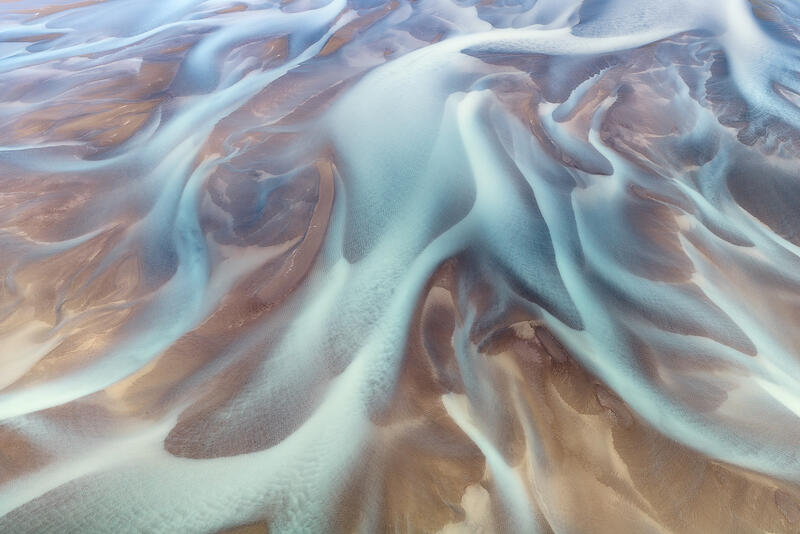 Soft turquoise glacial rivers flow across volcanic sands, creating an elegant natural abstract.