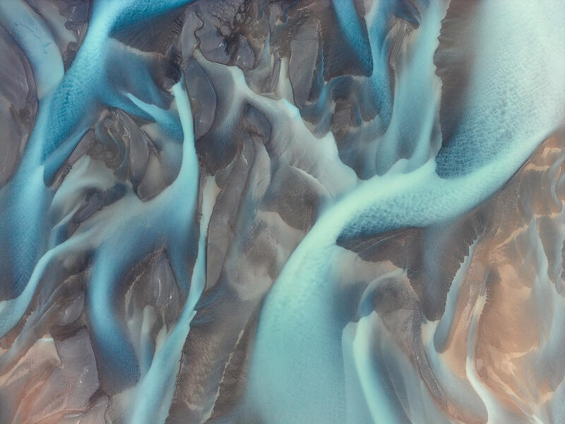 Aerial abstract of turquoise glacial rivers winding through volcanic sands in Iceland.