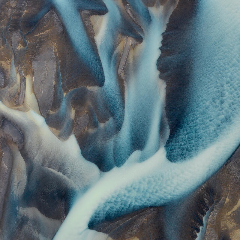 Abstract aerial of blue glacial river flowing through black volcanic sand in Iceland.