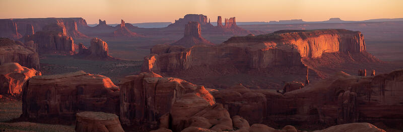 Iconic desert scene of monument valley with buttes and mesas as the sun rise side lights the scene from the right side.