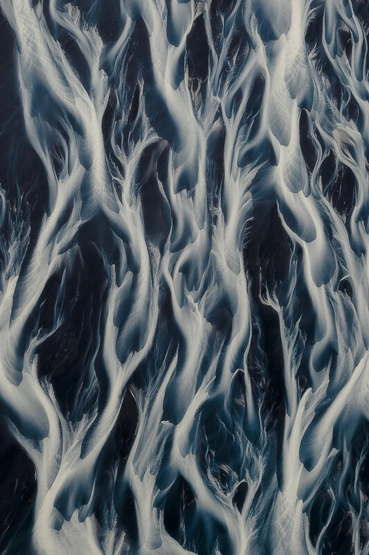 Minimal aerial abstract of braided glacial rivers over black volcanic sand.