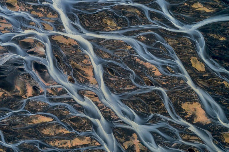Glacial rivers weave across volcanic plains like living arteries viewed from above.
