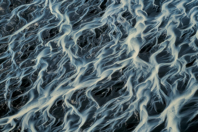An intricate network of braided glacial rivers forms an abstract pattern reminiscent of living neural pathways.