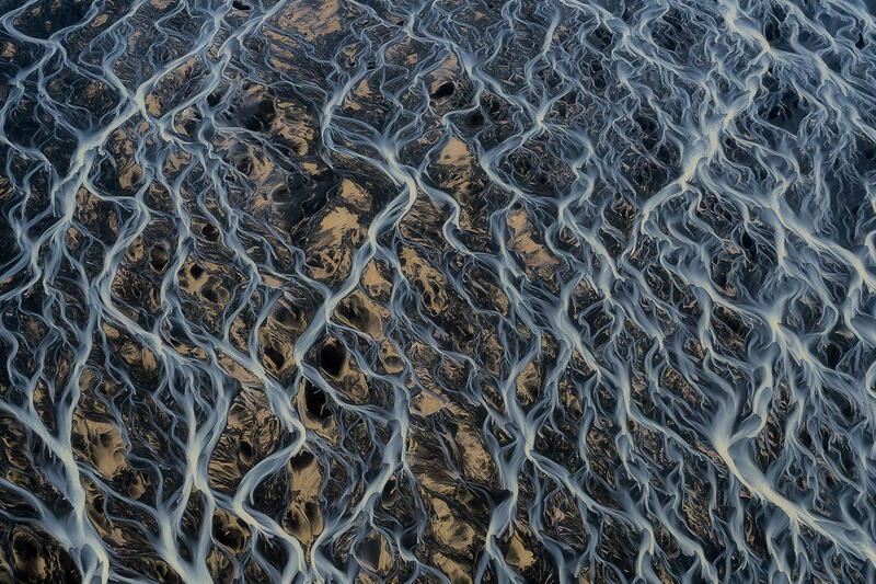 Aerial view of delicate braided river patterns resembling woven lace across Iceland's volcanic plains.