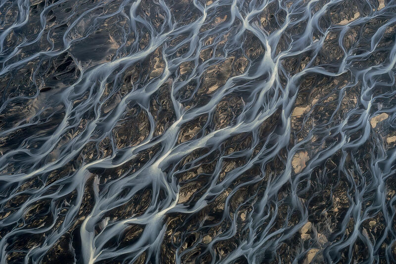 Intricate braided glacial rivers creating capillary patterns over volcanic sands in Iceland.