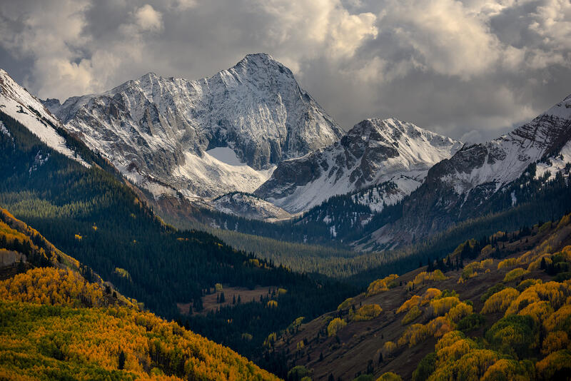 Fresh mountain snow rises above golden Colorado aspens where autumn and winter meet in the high country.
