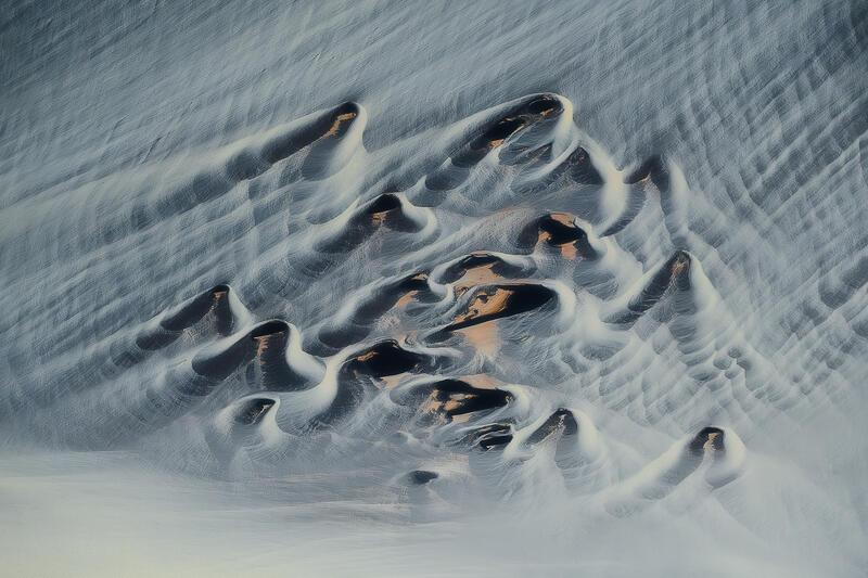Ancient volcanic forms appear to sleep beneath flowing layers of glacial sediment.
