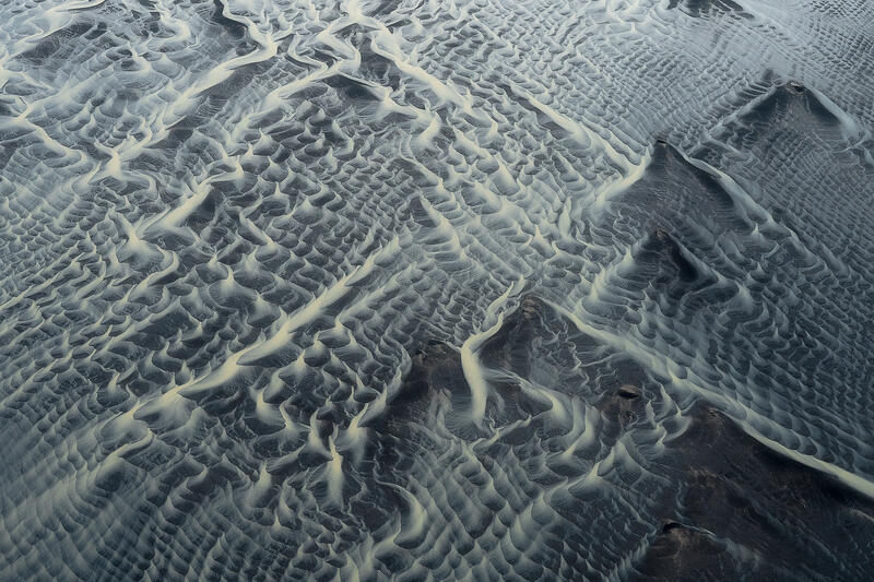 Aerial view of delicate braided river patterns resembling woven lace across Iceland's volcanic plains.
Alt Tag