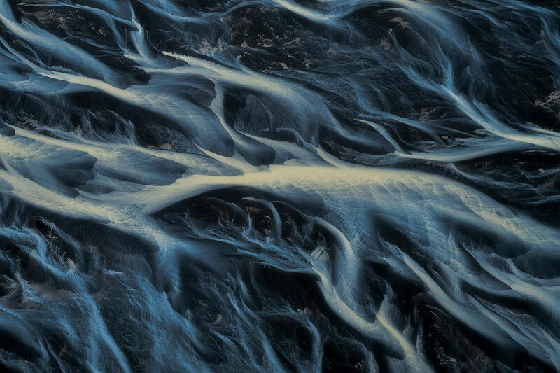 Minimal aerial abstract of braided glacial rivers over black volcanic sand.