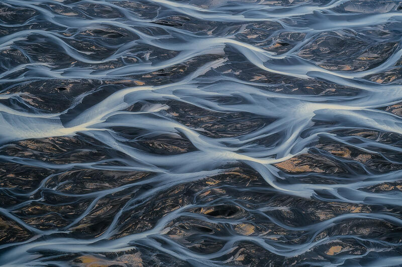 Aerial view of braided glacial rivers flowing across volcanic sands in Iceland.