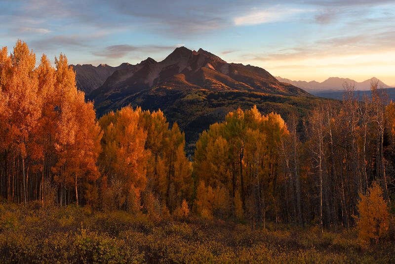 Golden aspens and warm evening light frame a dramatic Colorado mountain during peak autumn color.