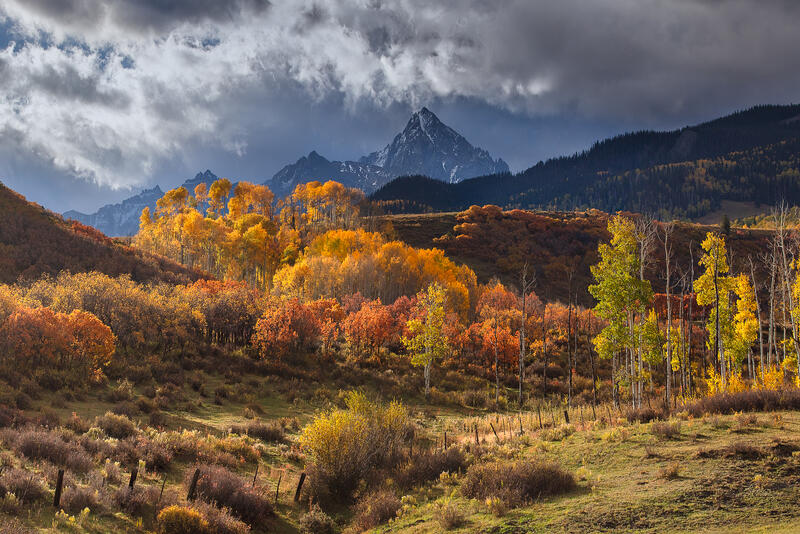 Breaking storm light illuminates brilliant autumn aspens beneath rugged peaks in the Colorado mountains.