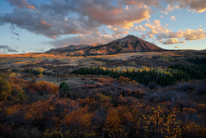 A Colorado mountain rises above layered autumn valleys under soft, shifting light.