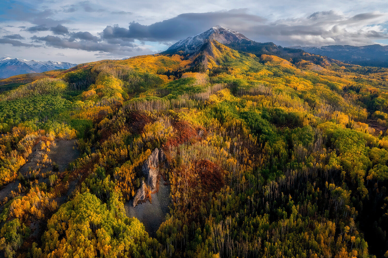 Mountain stands off in the distance surrounded by aspen trees in fall colors on hills descending from the mountain.