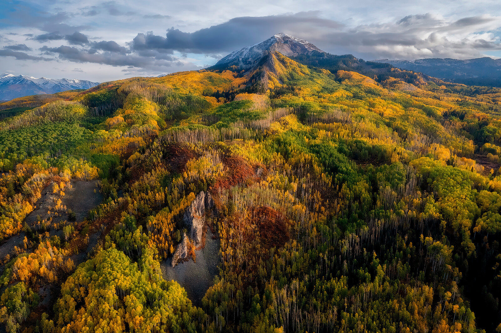 Ruby's Color Apron Mountain stands off in the distance surrounded by aspen trees in fall colors on hills descending from the mountain.