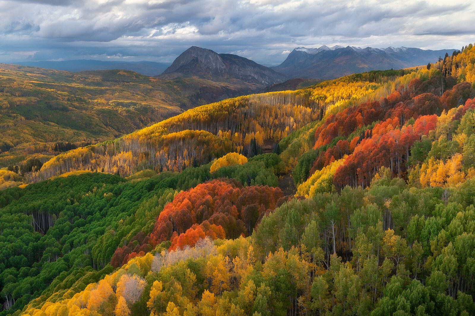 Mountains in the distance are surrounded with a valley of aspen trees in colors of red, yellow, green.