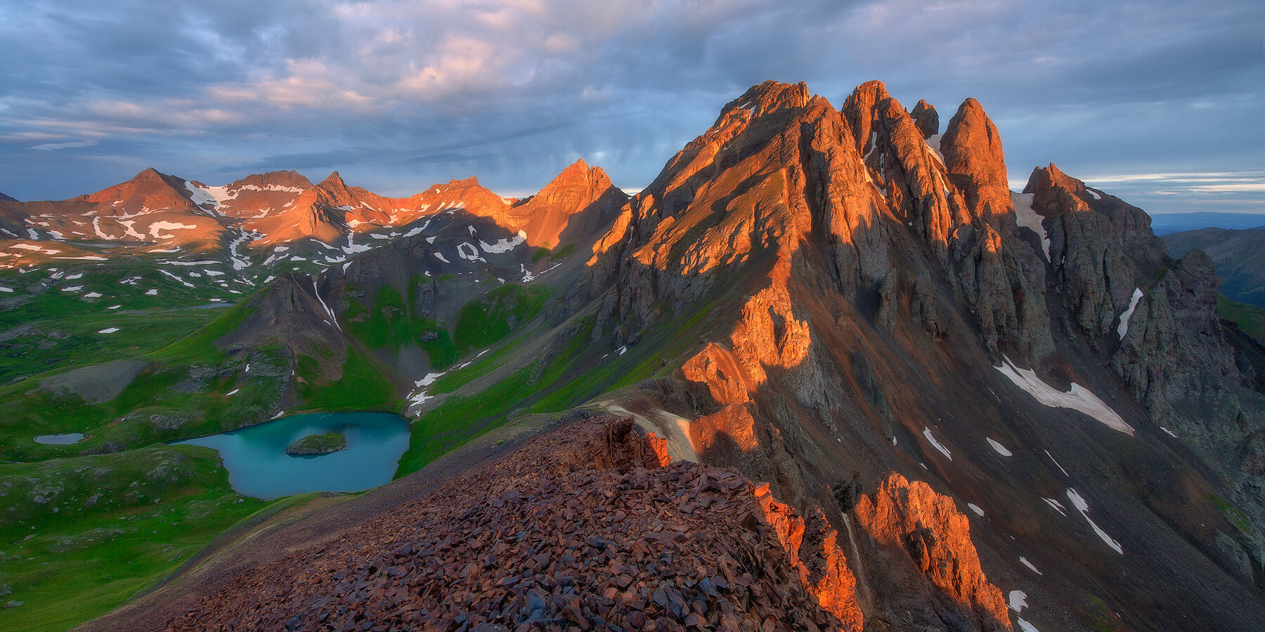 Sun lights up the top of the red mountains that cast a shadow on to a lake that reflects the entire sky and scene.