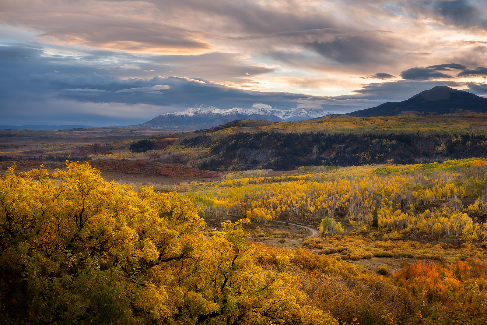 Fall colors flood the scene with orange and yellow and red with a snow covered mountain range in the distance.